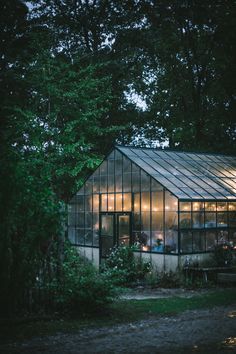 a glass house with lots of windows in the middle of some trees and bushes around it