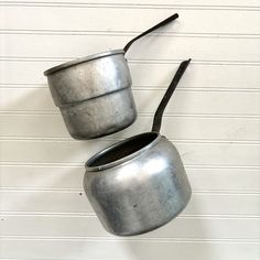 two metal pots hanging from the side of a wall