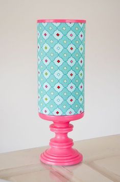 a pink candle holder sitting on top of a wooden table next to a white wall