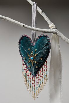 a heart shaped decoration hanging from a tree branch with beads and tassels on it