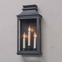 three candles are lit in an old - fashioned lantern on the side of a building