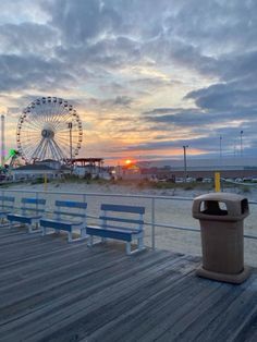 a boardwalk with benches and a large ferris wheel in the background at sunset or dawn