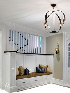 a room with some white cabinets and pillows on top of the bench in front of a window