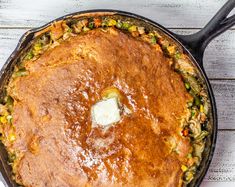 a skillet filled with food sitting on top of a white wooden table next to a spoon