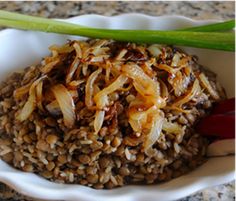 a white bowl filled with brown rice and onions on top of a marble countertop