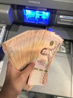 a person is holding cash in front of an atm machine with blue light on it