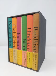 the four books are lined up in a book case on a white surface, one is brightly colored and the other is black