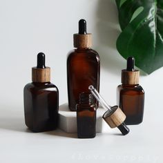 three brown glass bottles with wooden lids on a white surface next to a green plant