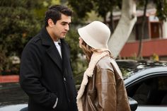 a man and woman standing next to each other in front of a car on the street