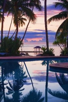 an empty swimming pool with palm trees and the ocean in the background at sunset or dawn