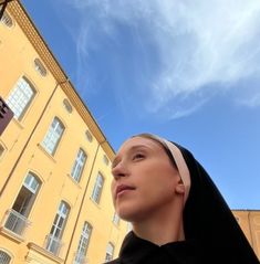 a woman wearing a nun outfit standing in front of a tall yellow building with windows