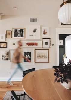 a man walking past a wooden table in front of pictures on the wall