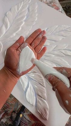 two hands are holding white paint on a piece of paper that has been carved into the shape of a feather