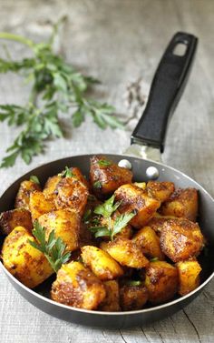 a pan filled with fried potatoes and herbs next to a knife on a wooden table