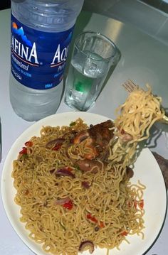 a white plate topped with noodles and veggies next to a bottle of water