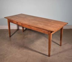 a wooden table sitting on top of a cement floor next to a white wall in an empty room