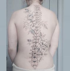 the back of a woman's body with flowers on it and an intricate cross tattoo