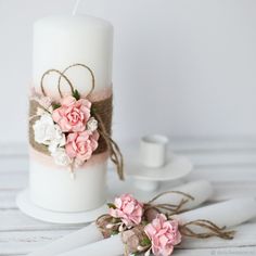 a white candle with pink flowers on it next to some napkins and a cup