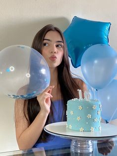 a woman holding balloons and a cake in front of her with blue decorations on it