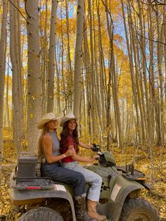 two women riding on the back of an atv through a forest filled with yellow leaves