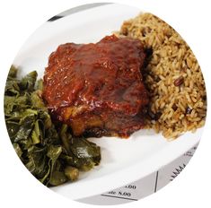 a white plate topped with meat and rice next to collard greens on a table