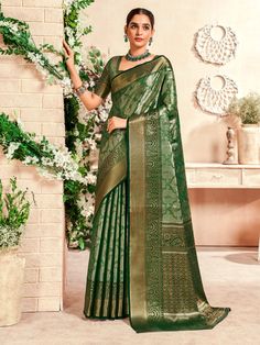 a woman in a green saree standing next to a wall with flowers and greenery