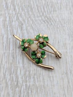 This pretty, lucky brooch features a group of shamrocks nestled within a gold tone metal wishbone. Each clover is covered in rich green enamel and has a brilliant clear rhinestone center. A luminous faux pearl sits atop the leafy cluster. The piece is in good condition. The enamel shows wear consistent with vintage jewelry. The stones and pearl are firmly in place, and the pin mechanism is fully functional. Take advantage of free domestic shipping! Floral Headpiece, Rich Green, Butterfly Brooch, Cat Brooch, Pearl Brooch, Mother Pearl, Green Enamel, Clear Rhinestones, Gold Tone Metal