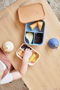 a child is eating some food from a container on the table next to an apple