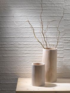 two white vases sitting on top of a wooden table next to a wall covered in textured paper