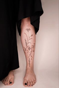 a woman's legs with tattoos and flowers on her left leg, in black dress