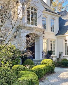 a large white house with lots of windows and bushes in front of it on a sunny day