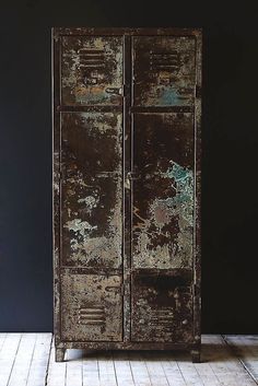 an old rusty metal cabinet sitting on top of a hard wood floor next to a black wall