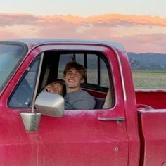 two people are sitting in the back of a red pick - up truck and smiling