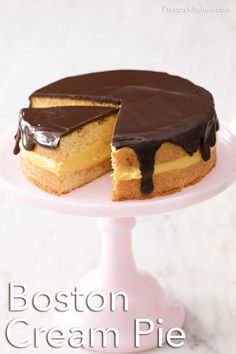 a boston cream pie on a pink cake stand with the slice cut out and ready to be eaten