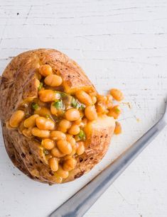 a baked potato filled with beans on top of a white surface next to a spoon