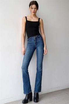 a woman standing in front of a white wall wearing blue jeans and black booties