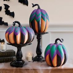 three painted pumpkins sitting on top of a table next to candles and books with bats in the background