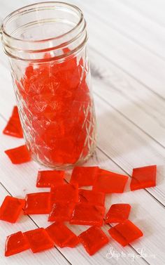 a jar filled with red gummy bears sitting on top of a white wooden table