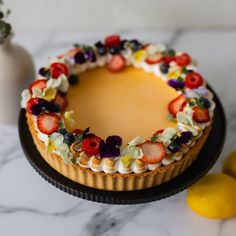 a cake decorated with fruit and flowers on a plate next to some lemons, strawberries, and other fruits