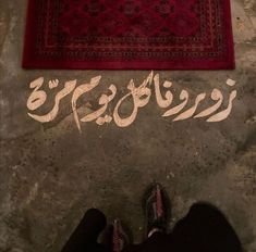 someone standing in front of a rug with arabic writing on the ground next to it