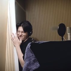 a woman with headphones is peeking out from behind a curtain and smiling at the camera