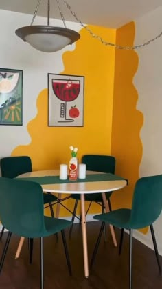 a dining room table with green chairs next to a yellow wall and pictures on the wall