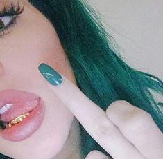 a close up of a person with green hair pointing to the side and wearing gold teeth