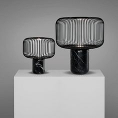 two black vases sitting next to each other on a white pedestal with grey background