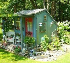 a small blue shed sitting in the middle of a lush green yard