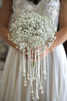 a woman in a white dress holding a bouquet of flowers with pearls hanging from it