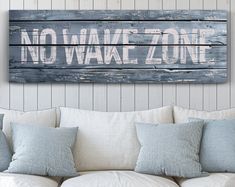 a wooden sign that says no wake zone hanging on the wall above a white couch