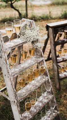 an old ladder filled with champagne glasses and flowers on top of it, sitting in the grass