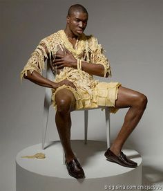 a man sitting on top of a white chair wearing a yellow shirt and shorts with his legs crossed