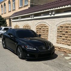 a black car parked on the side of a road next to a wall and building